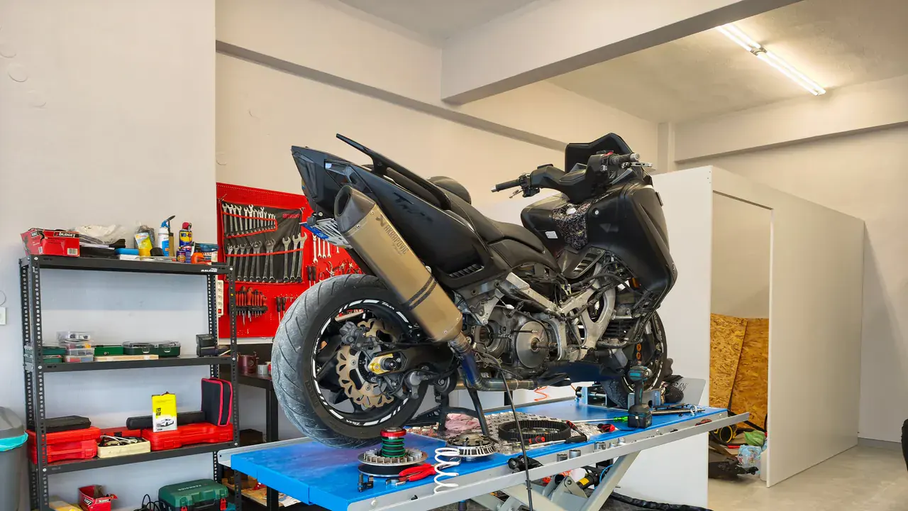A black scooter on a blue scissor lift, engine opened up and parts laid out on the deck.