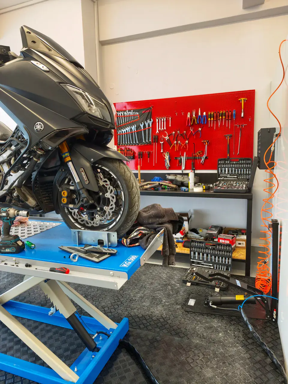The front wheel of a scooter on the blue lift. Behind it, the red tool wall.
