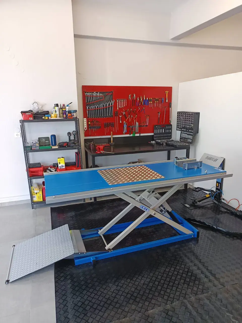 The scissor lift empty, ramp down, on black rubber matting.