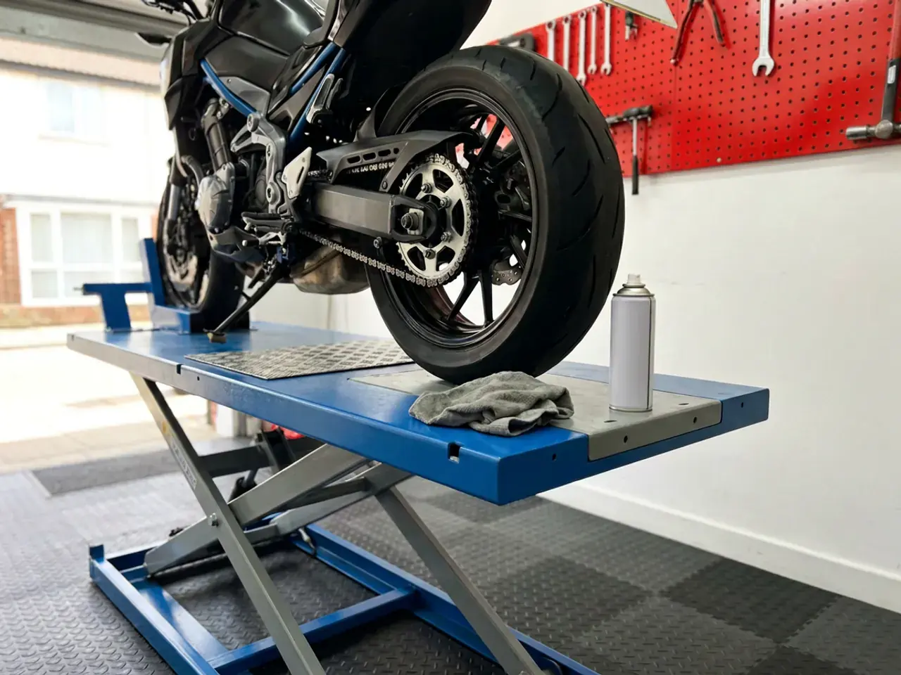 The rear wheel of a motorcycle on the lift, chain and sprocket clean and lubed.
