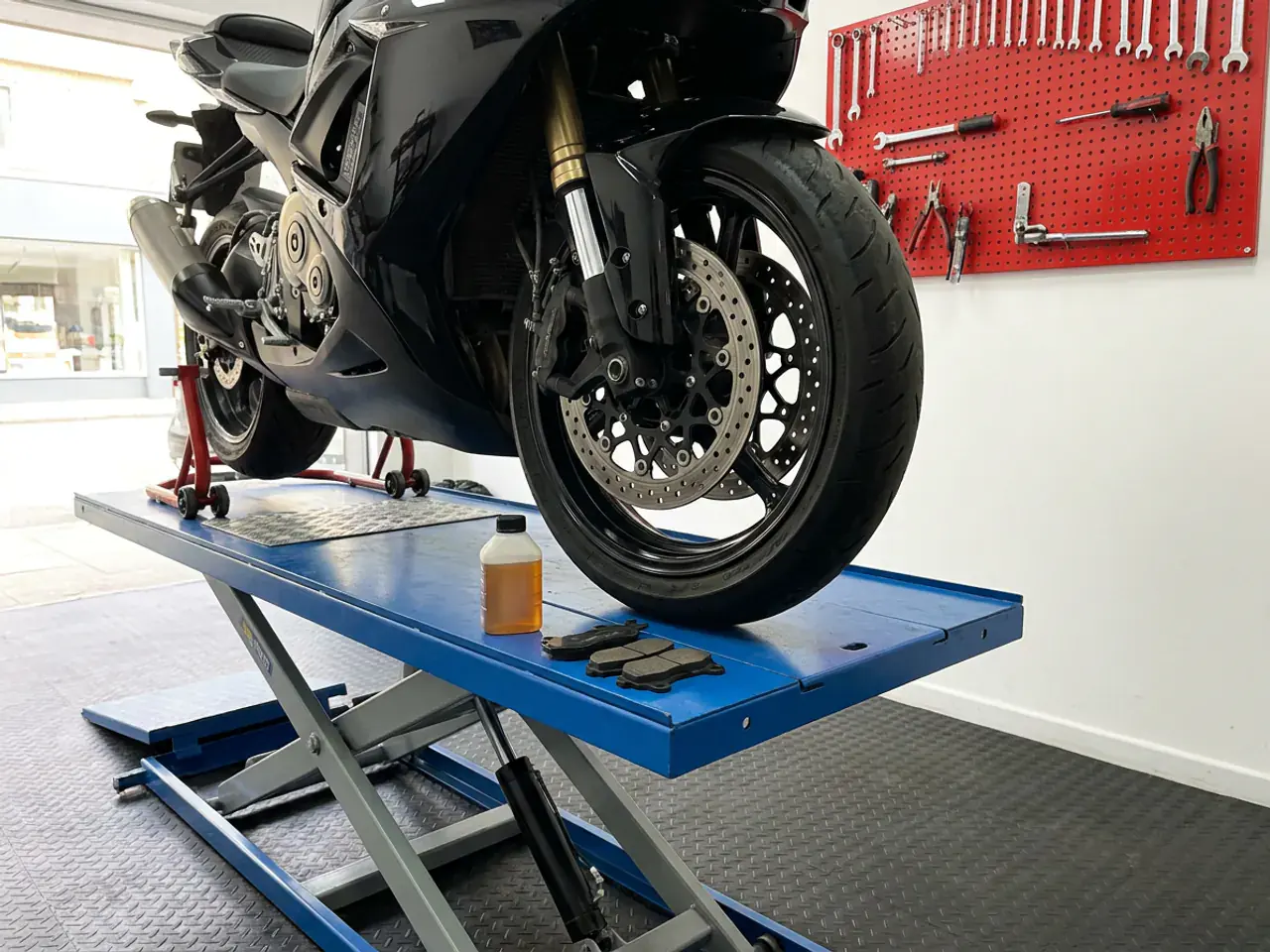 A motorcycle on the lift with new brake pads and brake fluid beside the front wheel.