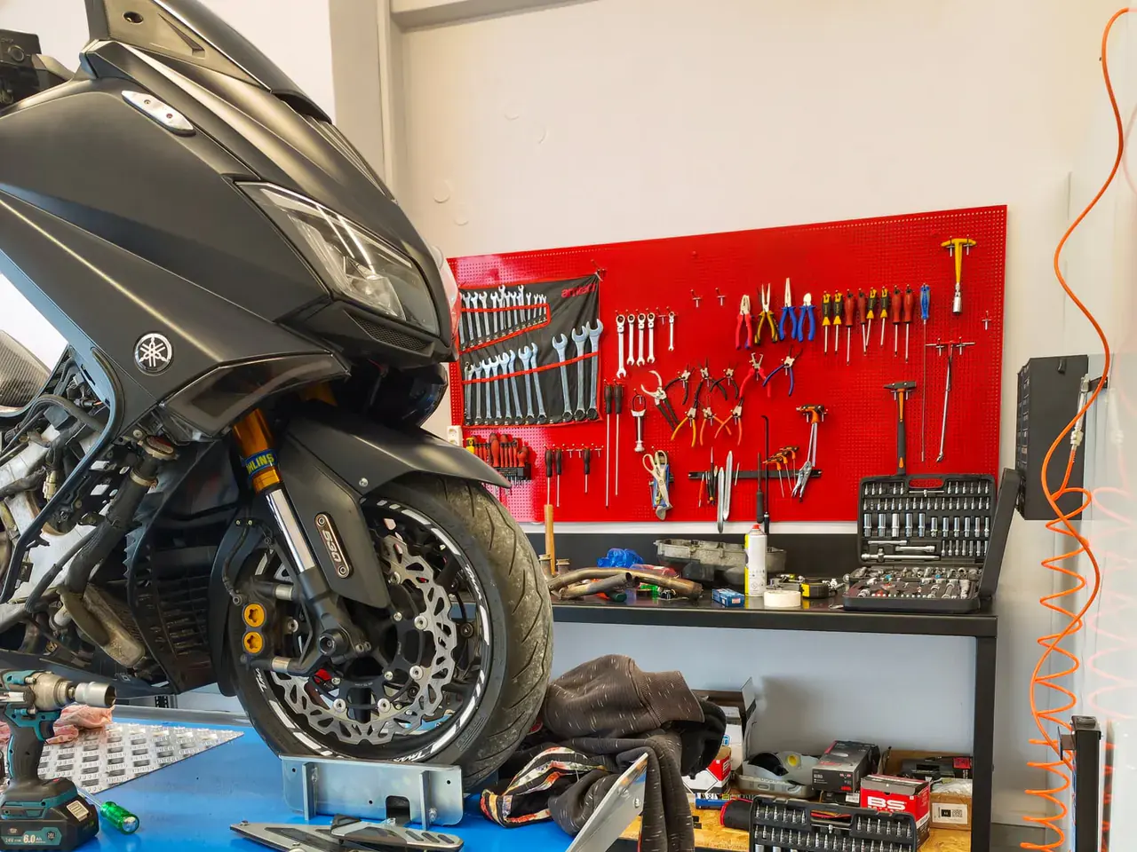 Μπροστινός τροχός scooter στο μπλε ανυψωτικό. Στο βάθος, το κόκκινο ταμπλό με τα εργαλεία.